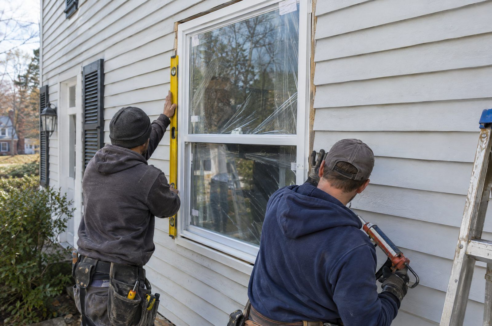 Two installers fitting a new white double-hung window into a clapboard wall