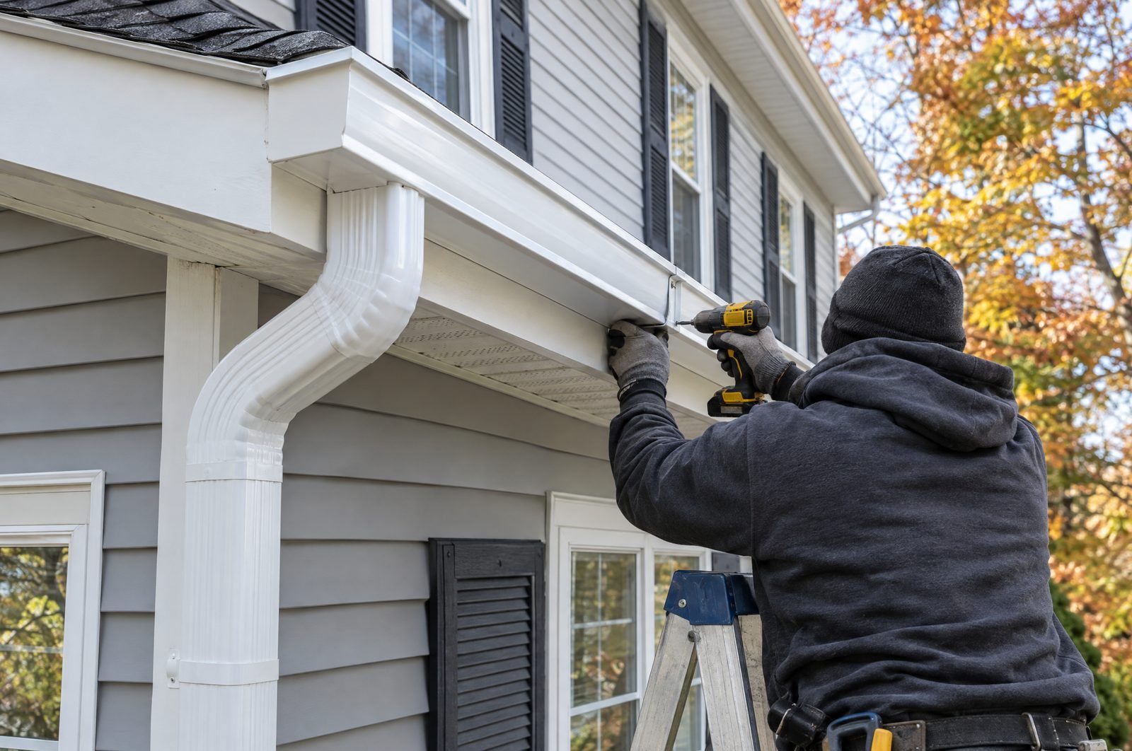 Installer fastening a new white seamless gutter along a home’s roof edge